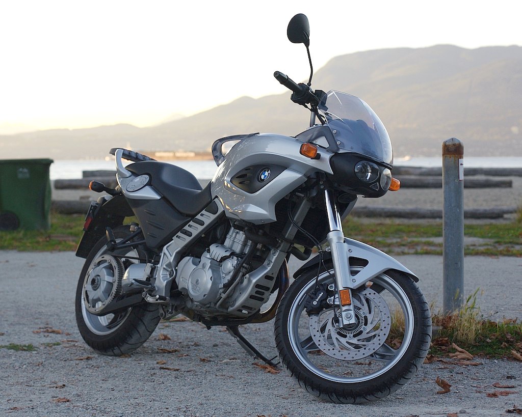 אופנוע BMW סילבר עם מנוע 1200, צילום צד קרוב על שטח אספלט, ברקע הים והררי הררי.