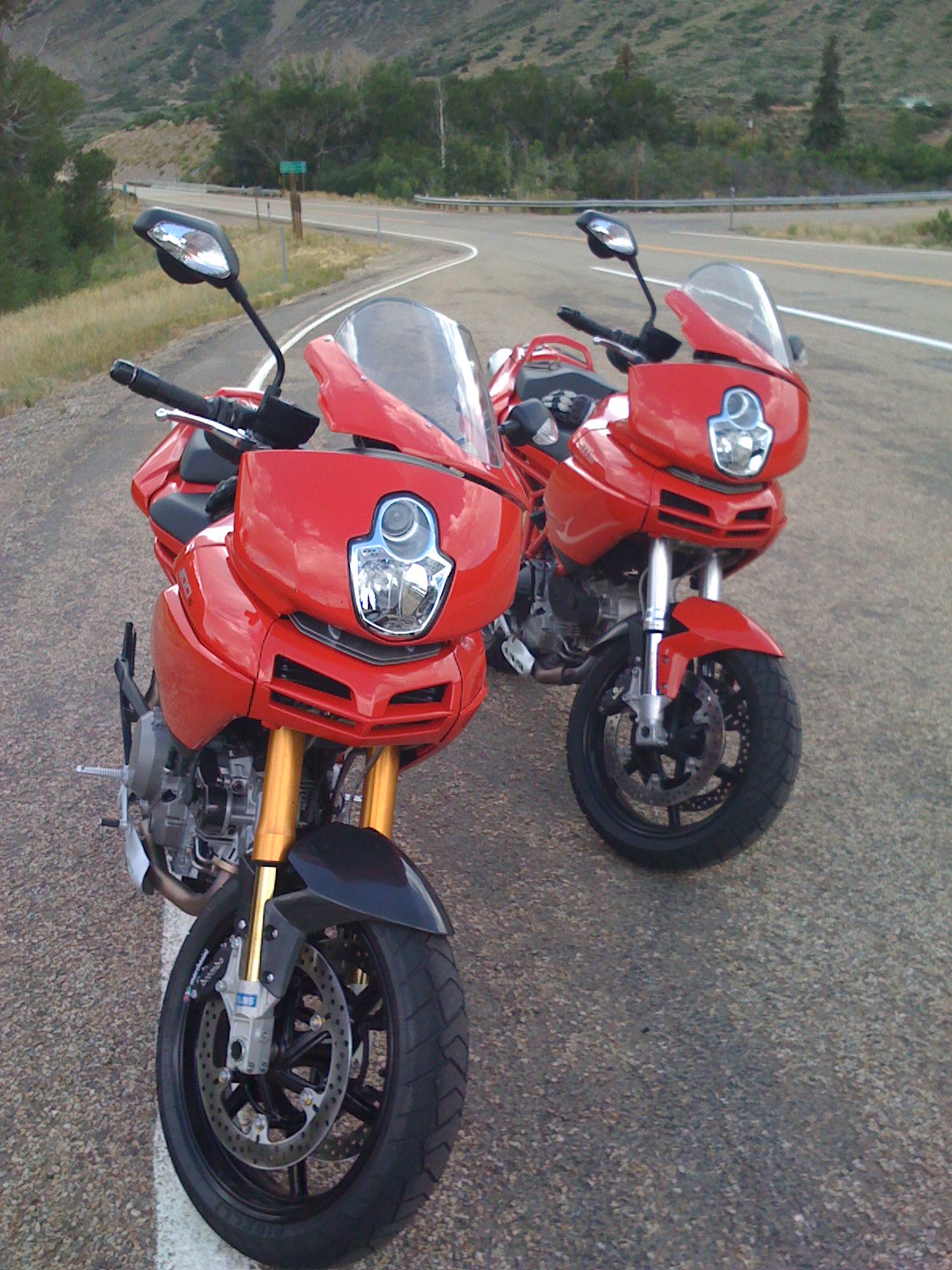אופנועי Ducati אדומים מונחים לצד כביש עקלתון, זווית קדמית עם מראה קדמי ורקע של הרים וצמחייה