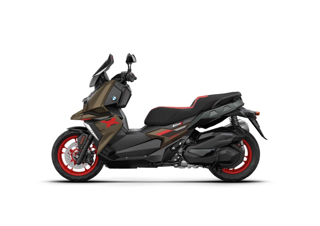 אופנוע BMW C400X בצבע שחור עם פסים אדומים, צילום צד, חנייה עירונית עם גדר אדום ברקע