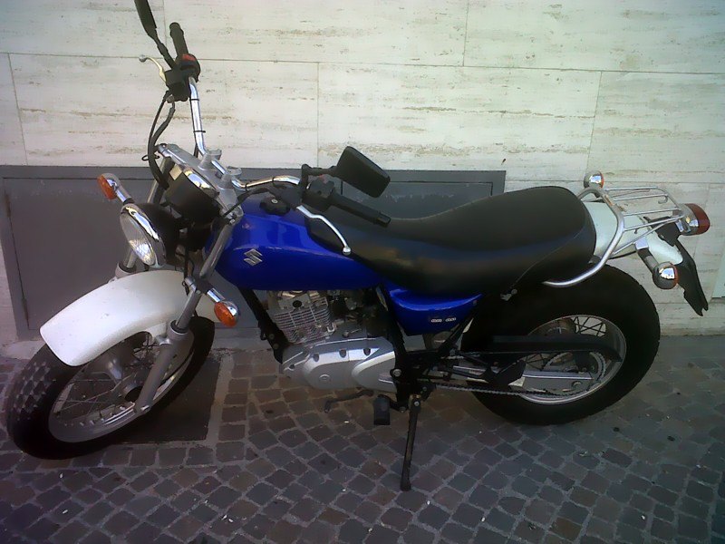 אופנוע סוזוקי כחול-לבן, דגם GSX, צילום צד, על רצפת אבן, מול קיר לבן