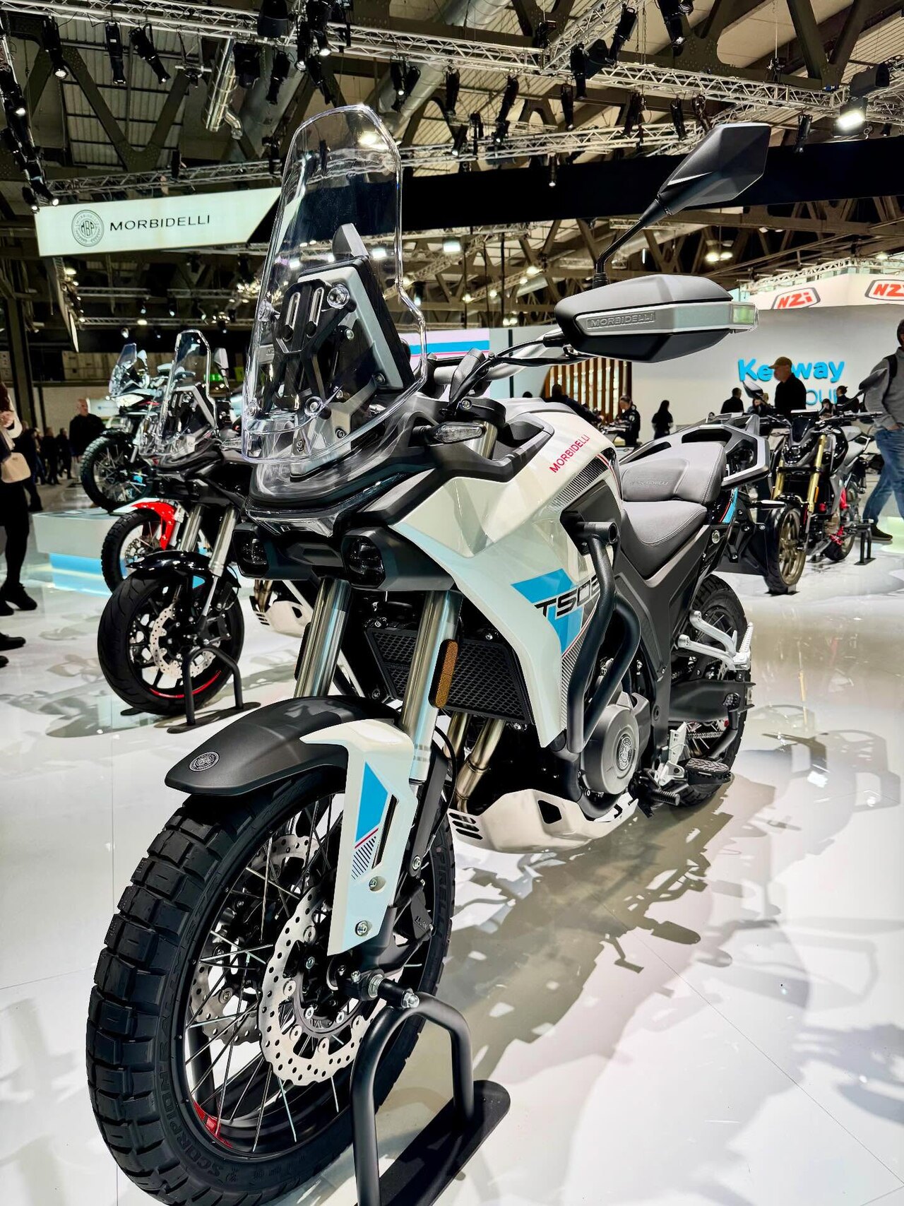 אופנוע Morbidelli T500 לבן-כחול בתצוגה, זווית קדמית, עם מראה וקרוסר, על רצפת תערוכה מבריקה