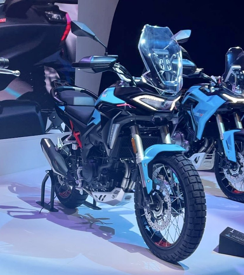 אופנוע KTM Adventure בצבע כחול בהיר, צולם מזווית קדמית-צדדית על במה בהירה, עם מראה זכוכית גדול וגלגלים לדרך לא מוגדרת.