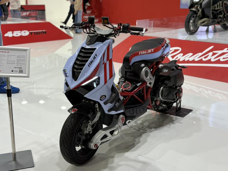 אופנוע חשמלי Italjet Roadster S בצבע לבן-אדום, צילום מזווית קדמית-צדית במعرض, עם מנוע חשוף ומסגרת אדומה