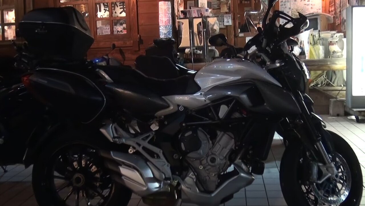 אופנוע Ducati דגם Multistrada בצבע אפור-שחור, צולם מזווית צדית בפנים חנות עם רקע עץ ופוסטרים.