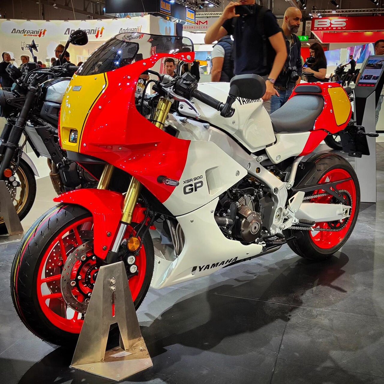 אופנוע ימבה XSR 900 GP בצבעים אדום, לבן וצהוב, צולם בזווית צדית בפינה של תערוכה, עם גלגלים אדומים ומסגרת מטאלית, סביבת