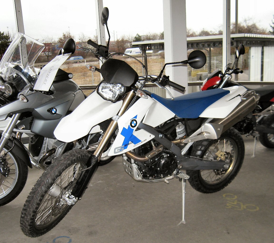 אופנוע BMW G 650 X Challenge לבן-כחול עם מושב כחול, מוצב בפינת מראה חיצונית, לצד אופנועים נוספים, זווית קדמית.
