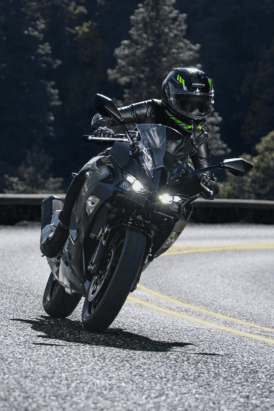 אופנוע Kawasaki Ninja כחול-לבן, צילום צד קדמי, עמיד על מדרכה עם עלים יבשים, מותג ודגם נראים בבירור