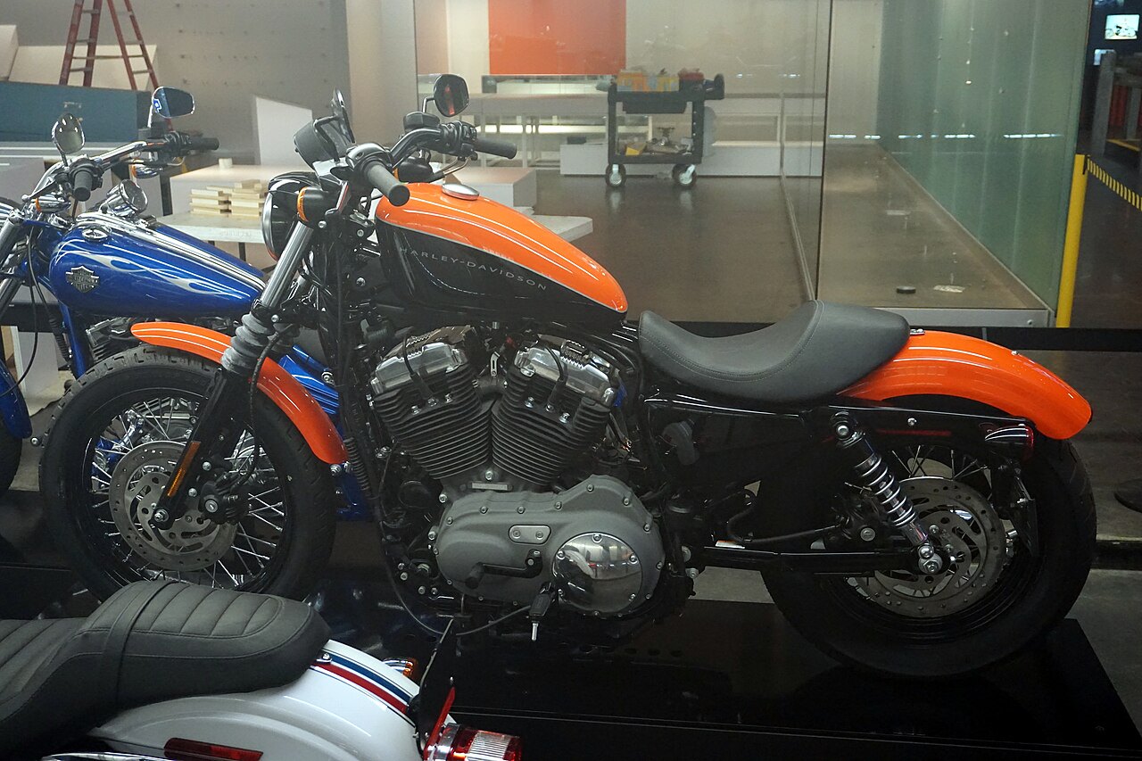 אופנוע Harley-Davidson בצבע כתום-שחור, צילום צד, בתצוגה פנימית עם אופנוע כחול ברקע