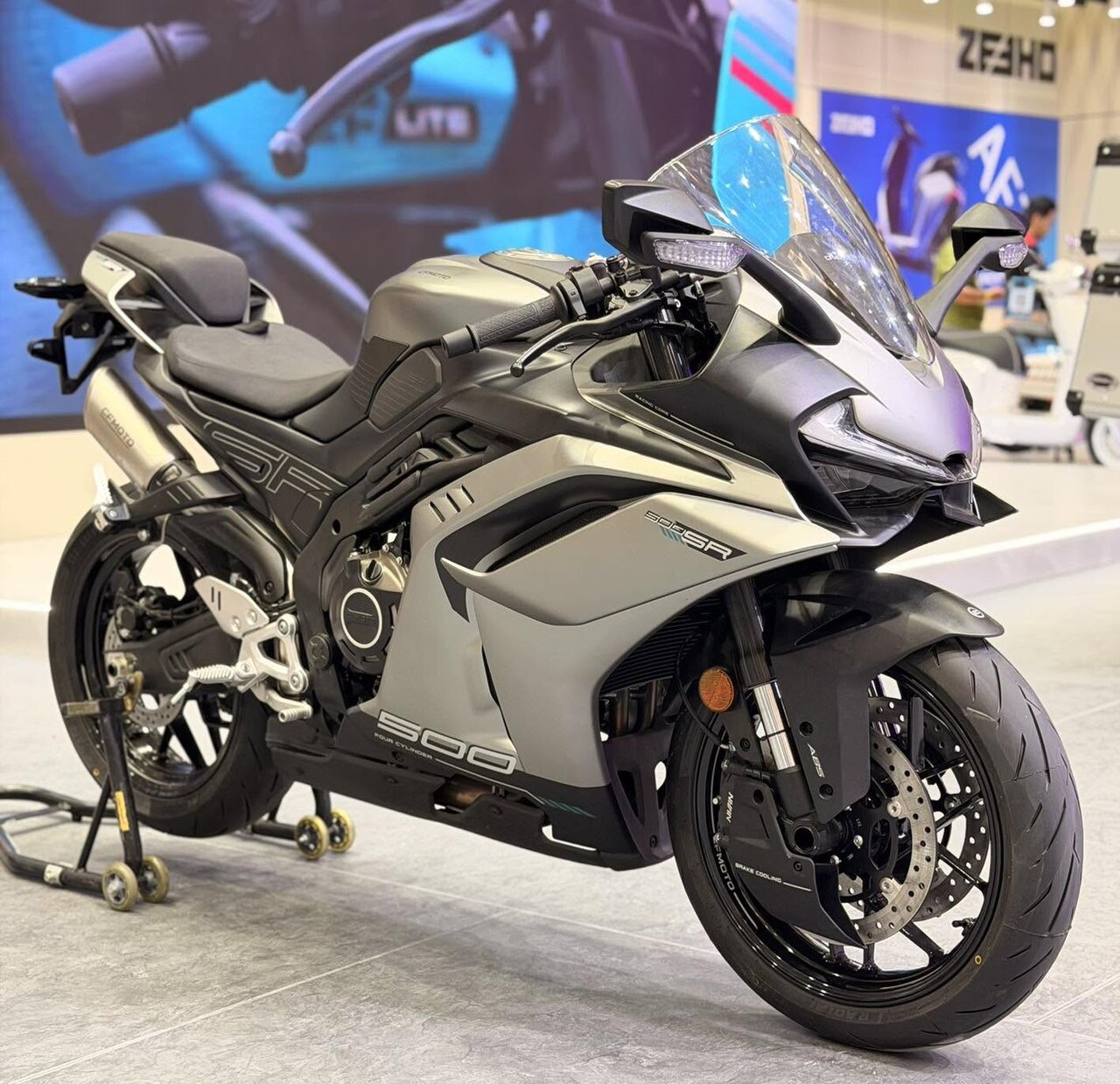 אופנוע ZEHO 500SR בצבע אפור-שחור, זווית צד, בתצוגה בתערוכה עם רקע של לוגו ZEHO ופרסומת אופנועים