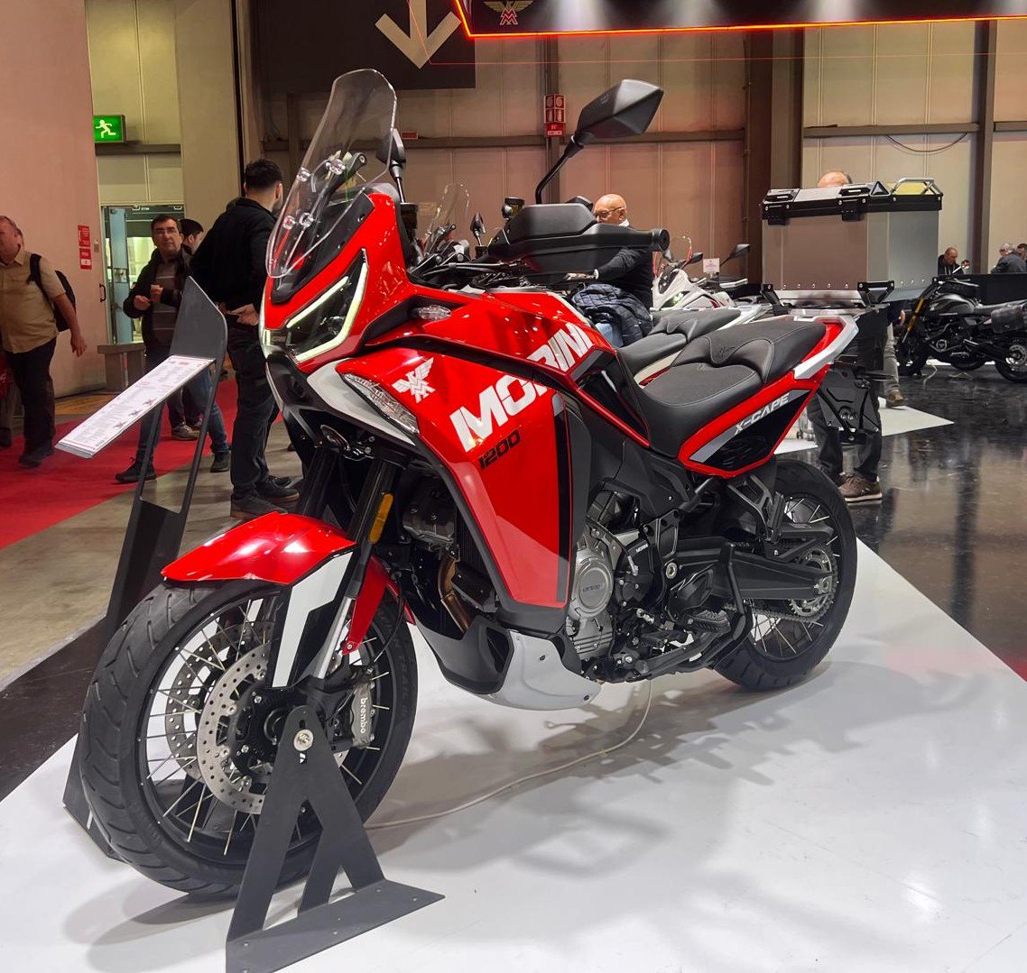אופנוע מוטורגיי 1200 אדום עם פנים שחורים, צילום צד מימין, בתצוגה פנימית עם מבקרים ברקע