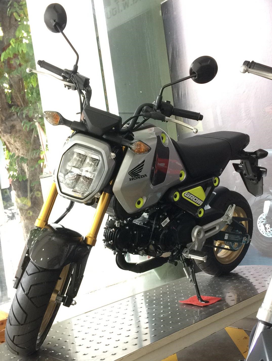 אופנוע הונדה GROM מודרני בצבע אפור עם פלטפורמה זהובה, צילום קרוב מזווית צדית-קדמית במבנה פנים, עם ספסל שחור וסימני מותג