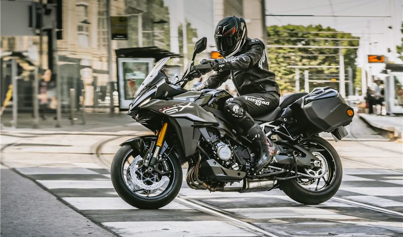 אופנוע Ducati Multistrada V4 S בצבע שחור עם פלטפורמות זהב, צילום מזווית קדמית מימין על כביש אבן, רקע של עצים עירומים.