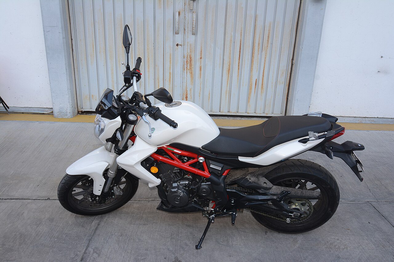 אופנוע Ducati Monster לבן עם מסגרת אדומה, צילום צד, על רצפת בטון מול דלת מתכת מוזהבת