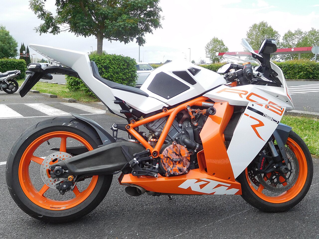 אופנוע KTM RC8 1190 לבן-כתום, צילום צד, מסגרת כתומה, מנוע חשוף, פארקינג עם עצים ברקע