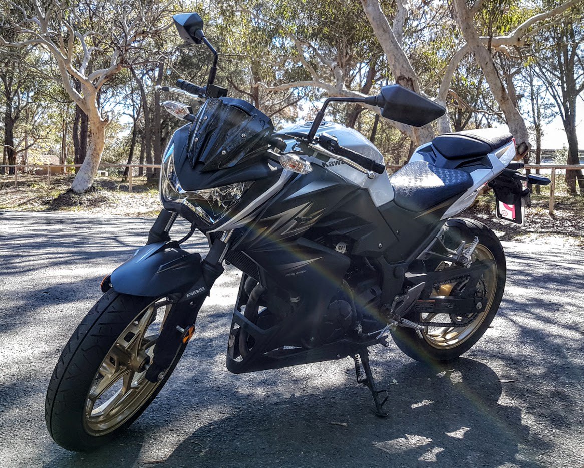 אופנוע קבצ'י Kawasaki Z650 בצבע כחול-אפור, צילום צד מימין על כביש עץ, עם מראה עץ וצללים