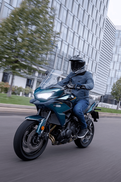 אופנוע Kawasaki אדום-לבן עם מארזים, צילום קרוב מזווית נמוכה, רקע של הר ענק בשלג תחת שמיים כחולים.