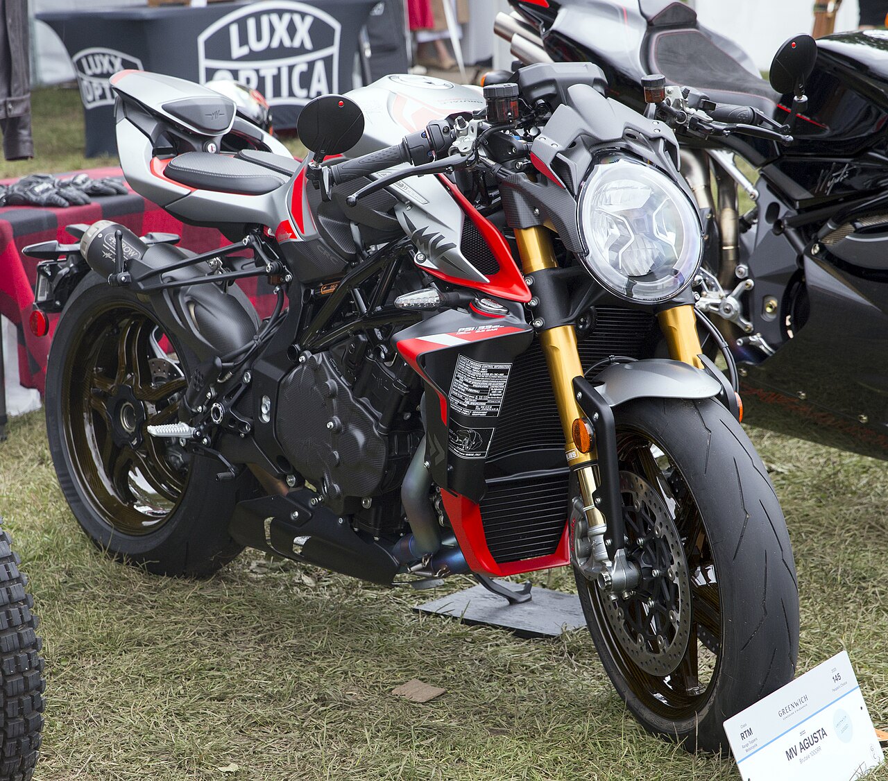 אופנוע MV Agusta בגרי, אדום וכסוף, מוצג בחצר על דשא, זווית צד קדמית, עם מותג ומדבקה של.GREENWICH