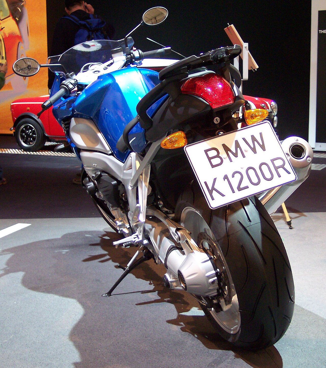 אופנוע BMW K1200R כחול-לבן, צילום מאחור, מוצג בתערוכה עם רכב אדום ברקע