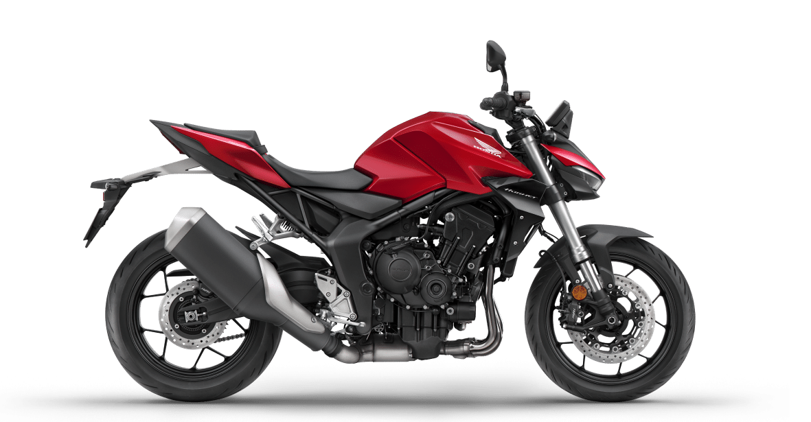 אופנוע הונדה CB1000 הורנט אדום מוצג בתערוכה, עם אישה במדים שחורים יושבת עליו, רקע של עמדת הונדה עם שלט מודרני.