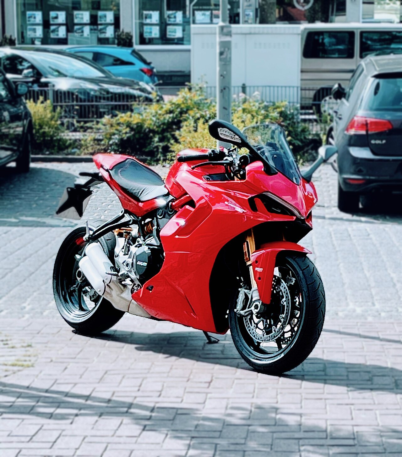 אופנוע ספורט אדום דגם Ducati, צילום צד מקרוב על רצפת אבן, סביבת עירונית עם מכוניות ברקע