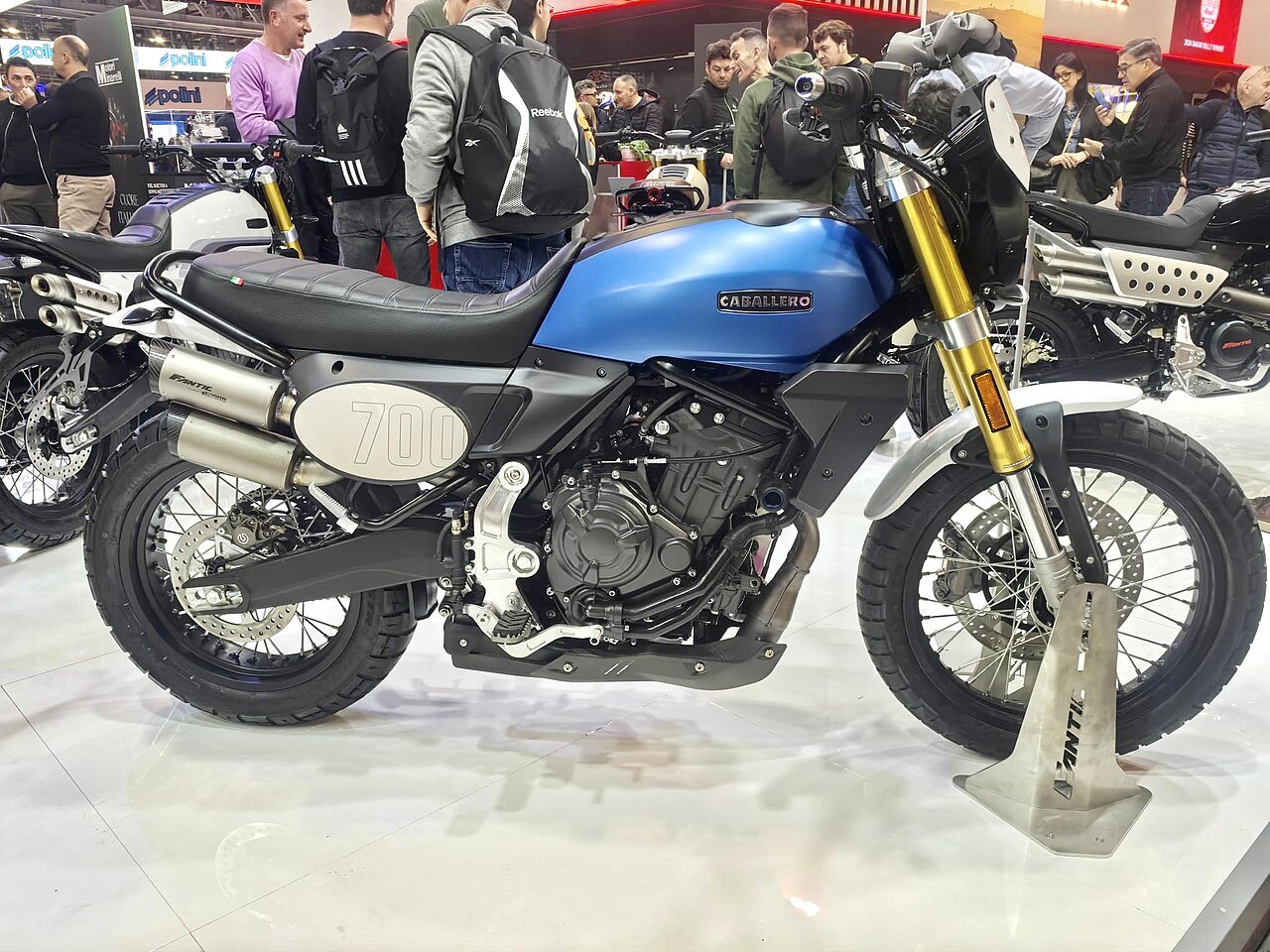 אופנוע Caballero 700 כחול עם מוטות זהב, צילום צד מקרוב בתצוגה, אנשים ברקע