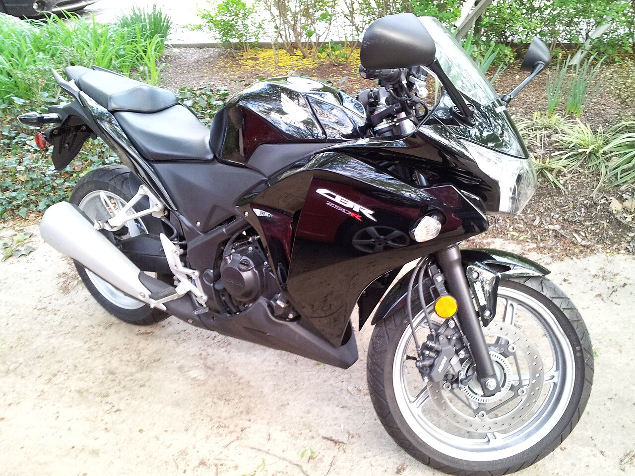 אופנוע הונדה CBR 250R שחור מונח בחצר עם צמחייה, צילום צד קדמי