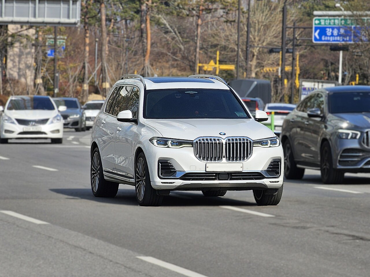 במוו X5 לבן בכביש עירוני, זווית קדמית, רכבים נוספים ברקע, שלט כיוון בקוריאנית