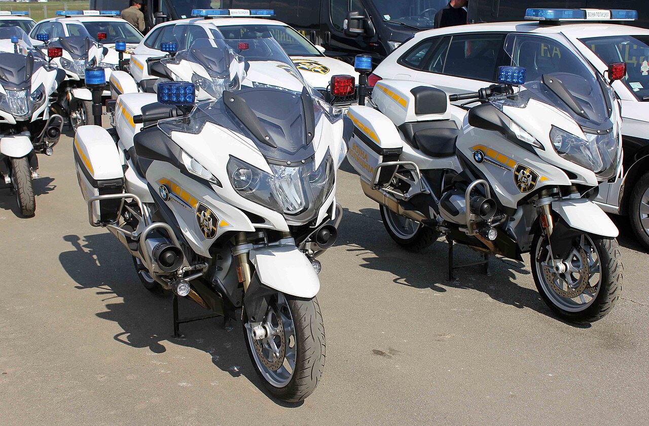 אופנועי BMW לבנים עם סימון משטרה, צולמים מקרוב בזווית קדמית, על רקע רכבים לבנים עם אורות חירום.