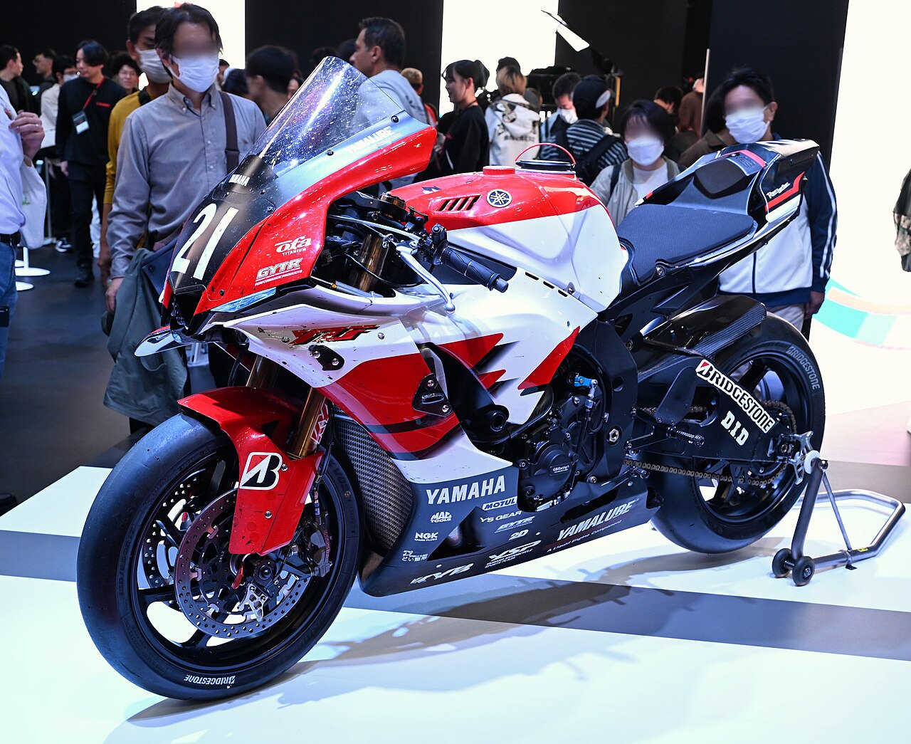 אופנוע מרוץ ימאה YZF-R1M אדום-לבן עם מספר 21, מוצג בתערוכה עם קהל ברקע
