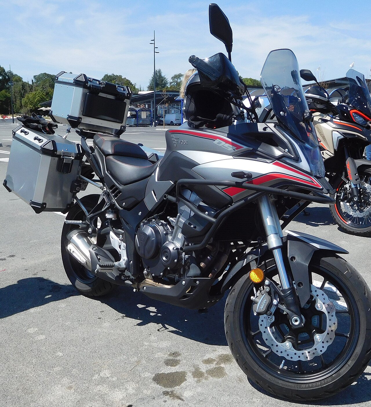 אופנוע Ducati Multistrada V4S אפור-שחור עם פסים אדומים, מונח בחצר חיצונית עם מזוודות מתכת, תצפית צדית מקרוב.