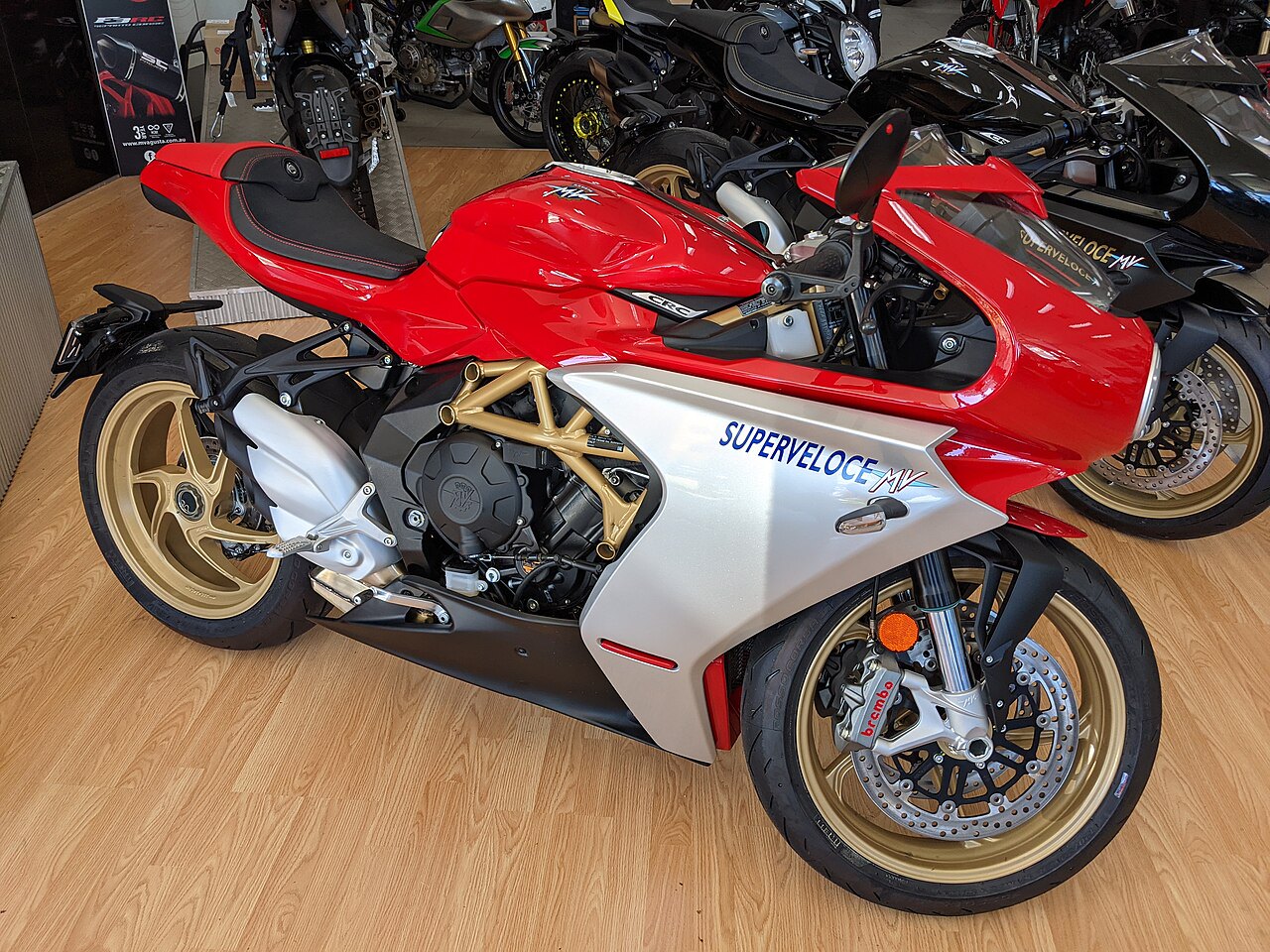 אופנוע MV Agusta Superveloce אדום-כסוף, זווית צד, פנים חנות עם אופנועים נוספים ברקע