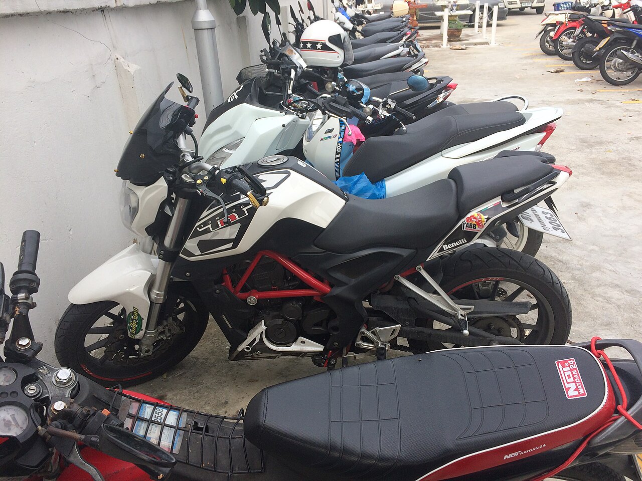 אופנוע לבן-שחור דגם Benelli עם מסגרת אדומה, מונח בשורה של אופנועים מול קיר לבן, עם מושב שחור ותווית NFI NATDAN 24