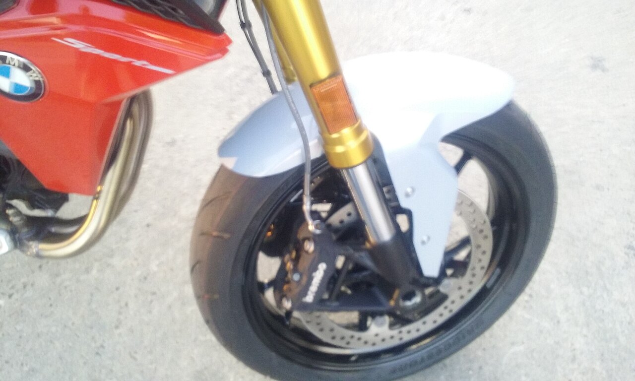 אופנוע BMW אדום עם מוט קדמי זהב וגלגל קדמי לבן, צילום קרוב של חלק הקדמי על רצפת בטון