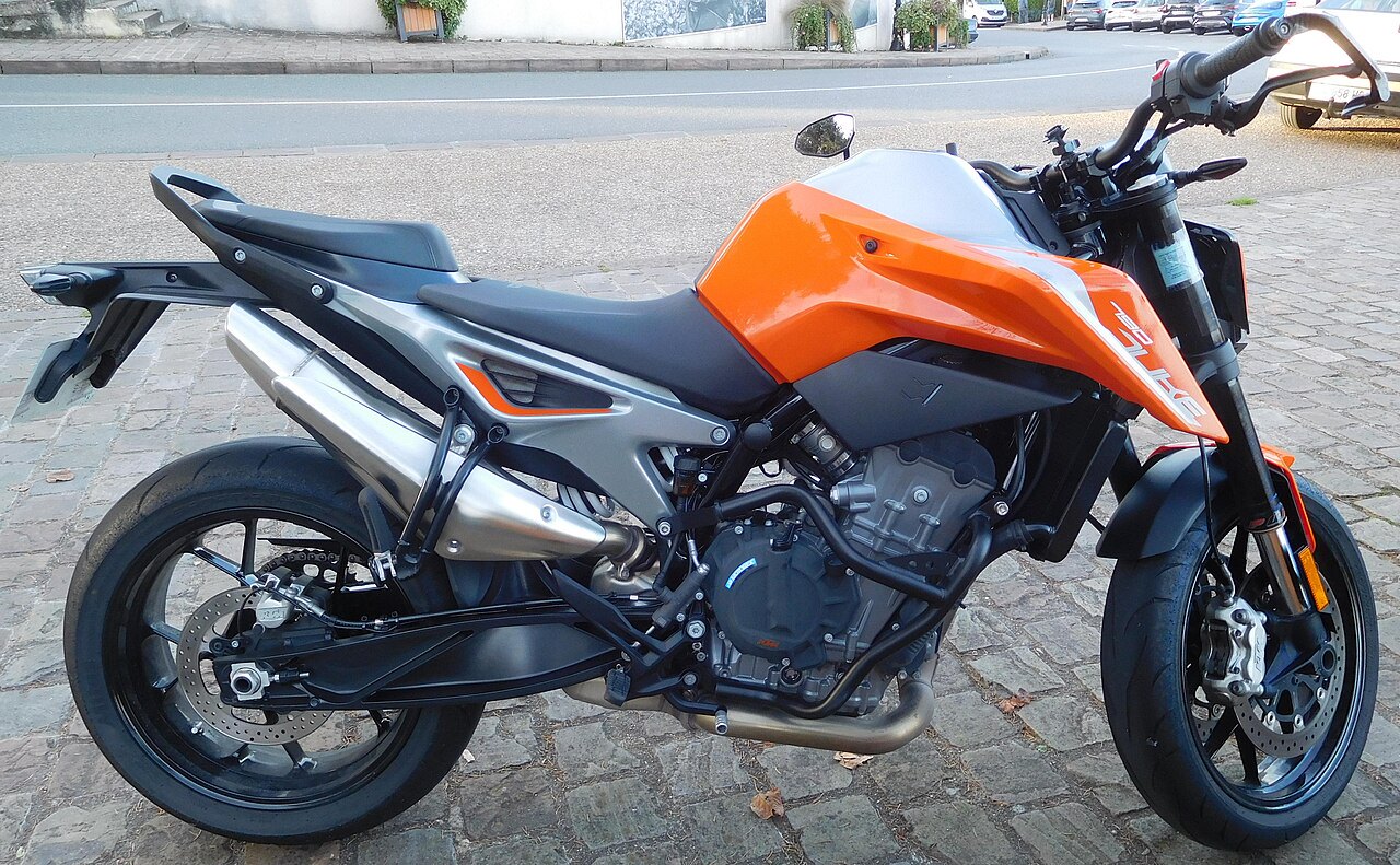 אופנוע KTM Duke 390 בצבע כתום-שחור, צילום צד, עמיד על שטח אבן, ברקע רחוב עירוני