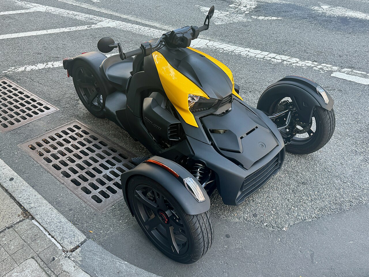 אופנוע תלת-גלגלי Can-Am Spyder בצבע שחור-צהוב, צילום מלמעלה על כביש עירוני עם חצייה ומערכת تصريف.