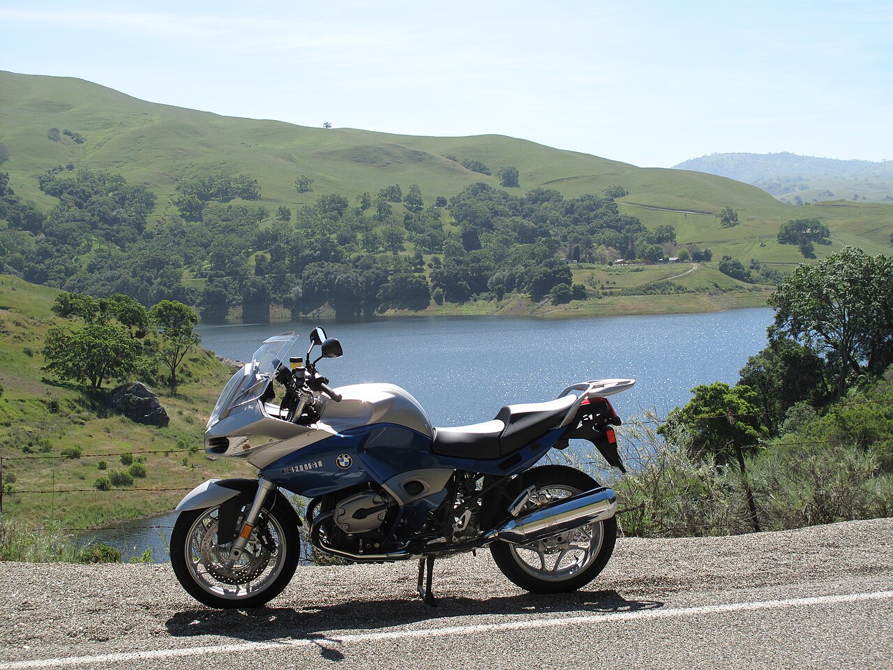 אופנוע BMW R1200RT כחול-לבן מונח על כביש, צילום צד, ברקע אגם ורמות ירוקות