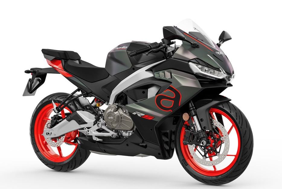 אופנוע אפריליה RS 660 לבן-שחור עם גלגלים אדומים, צילום צד, על מדרכה אבן מול בית עם שיחים ירוקים