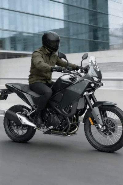 אופנוע Kawasaki KLE 500 לבן-ירוק בתצוגה, זווית צד, עם גלגלים שטח וקופסה אחורי, סביבת מعرض עם מבקרים.