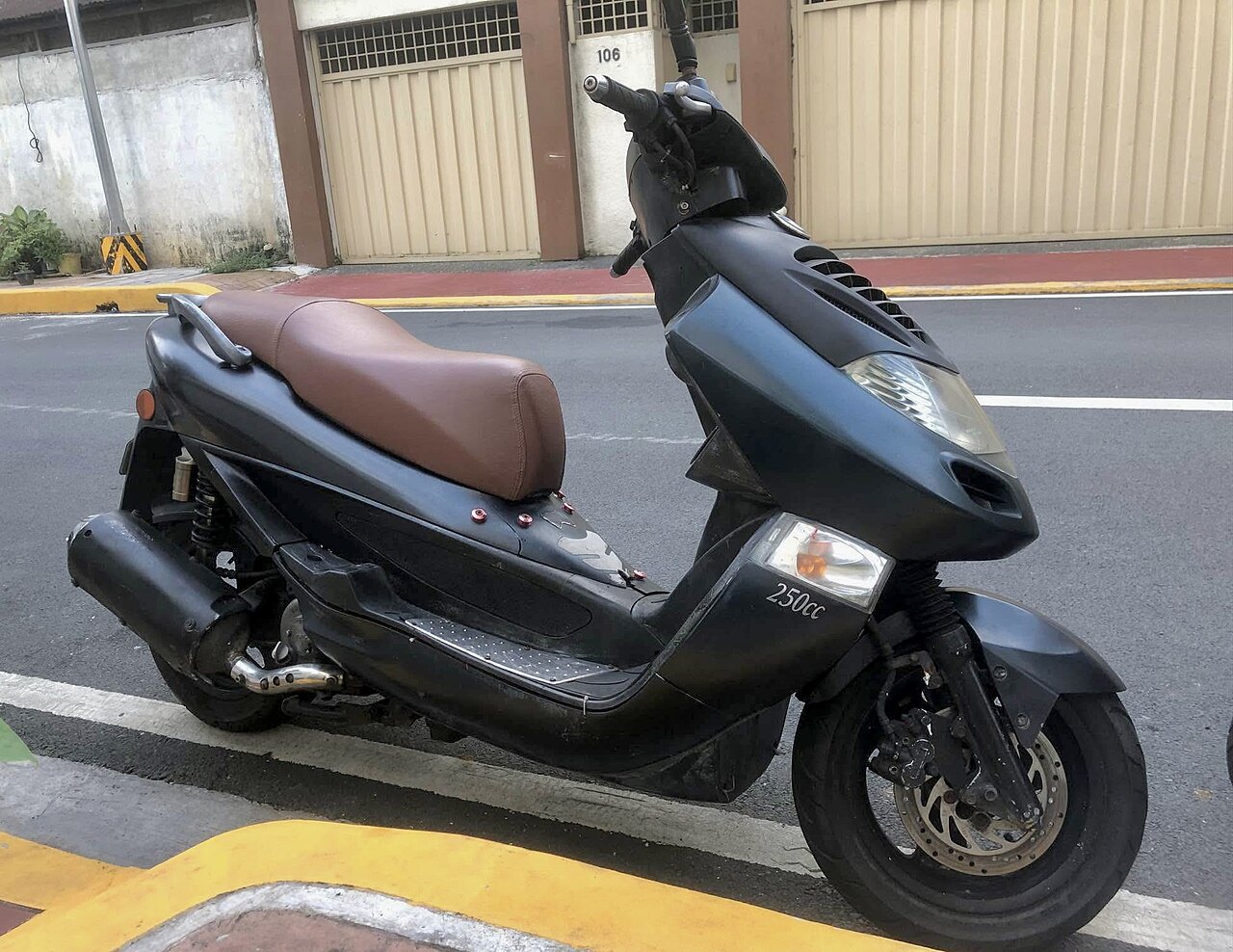אופנוע סקוטר שחור עם מושב חום, זווית צד, 250cc, חנייה ברחוב עם שערים חומים ברקע