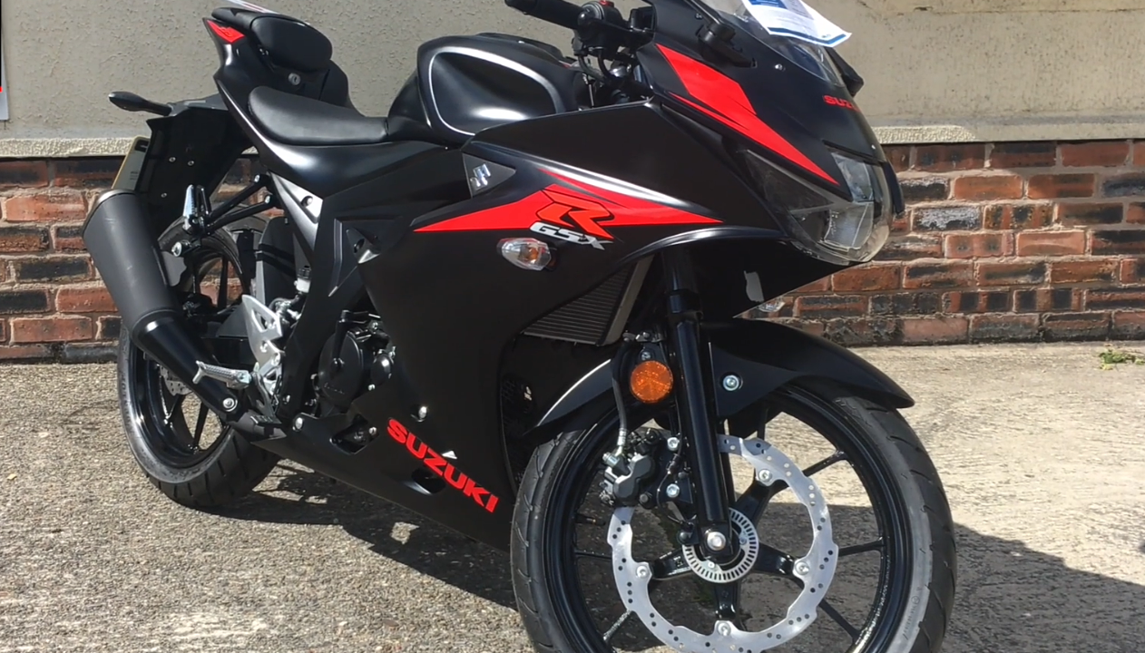 אופנוע סוזוקי GSX-R שחור עם פסים אדומים, צילום צד ימין על רקע חומה אבן, מותג ודגם נראים בבירור