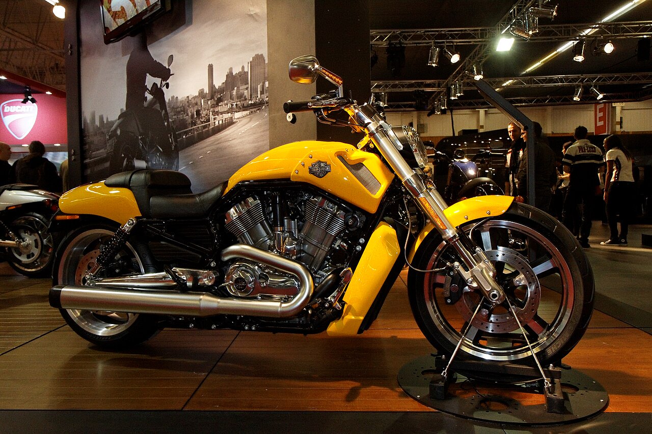 אופנוע Harley-Davidson צהוב בהיר, דגם כביש, בתצוגה פנימית עם מראה פנימי וגלגלים גדולים, על רקע של מודל עירוני שחור-לבן.