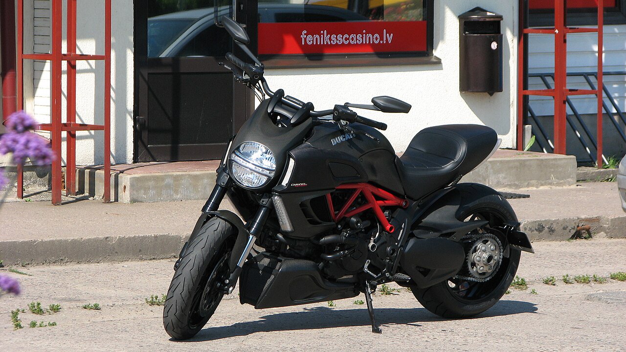 אופנוע דוקאטי דיאבל שחור עם מסגרת אדומה, צילום צד מימין, חוץ מול בניין עם שלט fenikscasino.lv