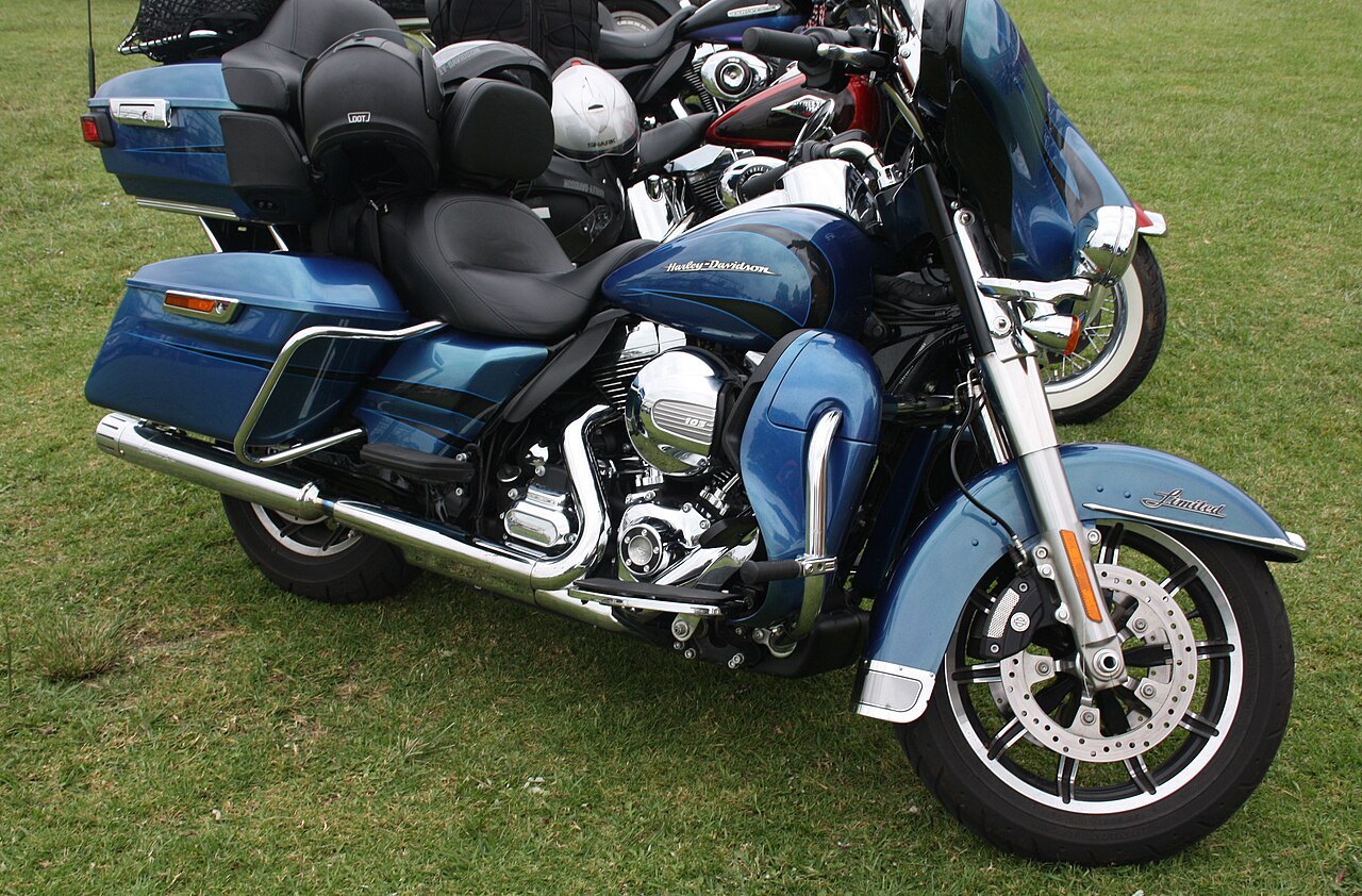 אופנוע Harley-Davidson Limited כחול בהיר עם מנוע 103, מושב זוגי, מזוודות צד, מצלבת חלולה, צילום מזווית צד על דשא ירוק.