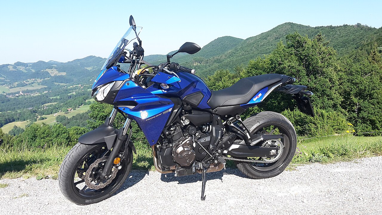 אופנוע יאמה XSR 900 כחול מונח על כביש אספלט עם נוף הרים ירוקים ברקע