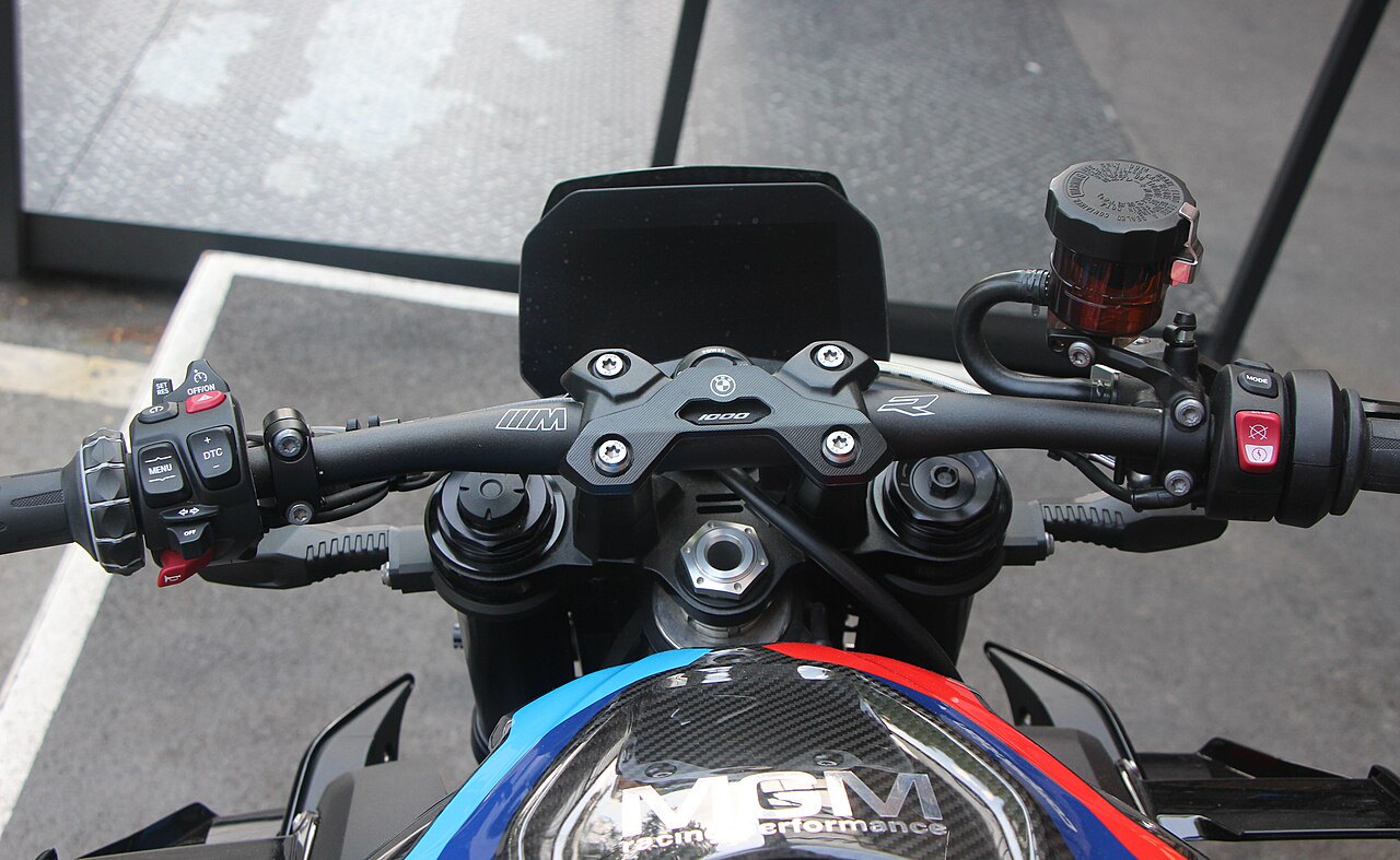 אופנוע BMW S1000RR בצבעי כחול ואדום, צילום מקרוב של מושך הידיות עם לוגו MGP Performance ופרטים טכנולוגיים, על רקע אספלט.