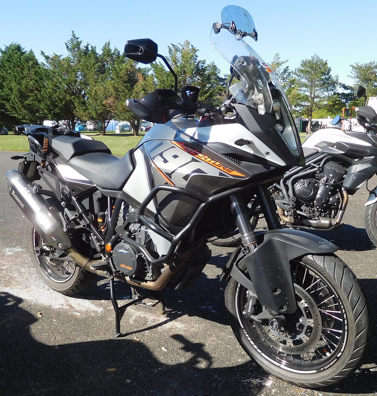 אופנוע KTM Adventure אפור-שחור עם מגן עיניים ומסגרת חימום, צולם בחצר פתוחה עם עצים ברקע