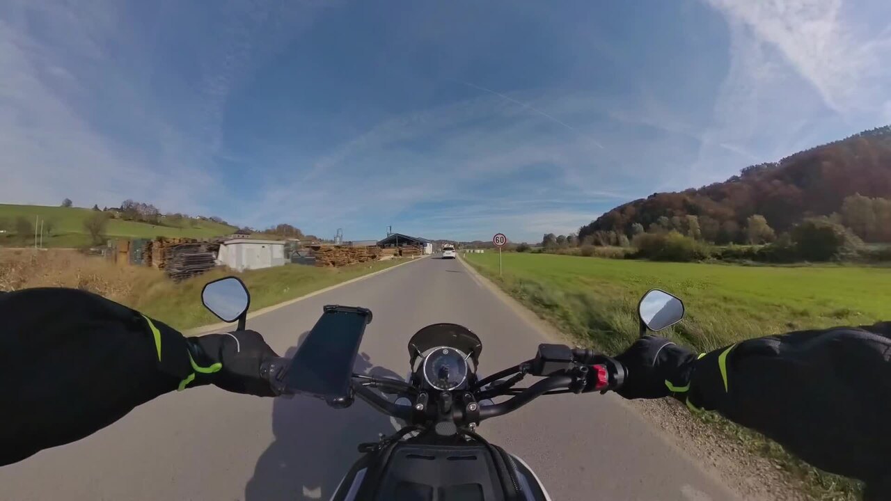 אופנוע שחור מותג Ducati נסיעת על כביש כפרי, זווית ראש, נוף שדות ירוקים ורמות, שמיים כחולים